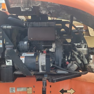 Open engine hood of an orange vehicle showing a dark diesel engine with multiple components and wiring