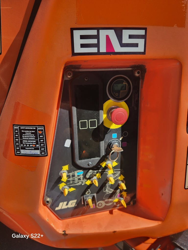 Close-up of orange industrial equipment control panel with EMS logo, emergency stop button, and safety labels