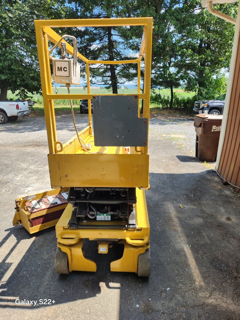 Yellow scissor lift with open platform and hydraulic mechanism, parked outdoors