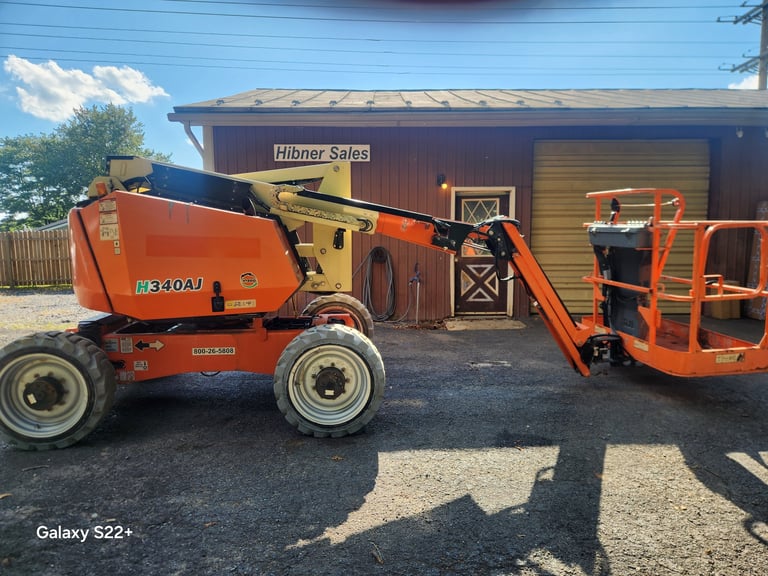 Two orange boom lifts parked in front of Hibner Sales building on gravel lot
