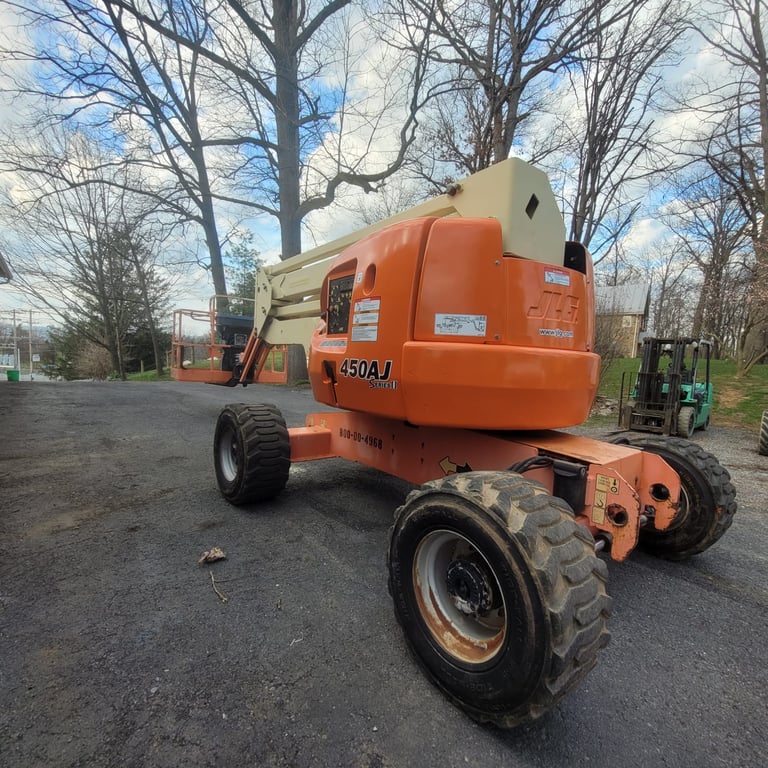 Orange and cream articulating boom lift parked on asphalt with bare trees in background