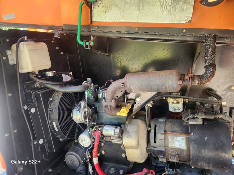 Internal engine compartment of machinery showing motor, hoses, pulleys, and cooling fan with orange exterior visible