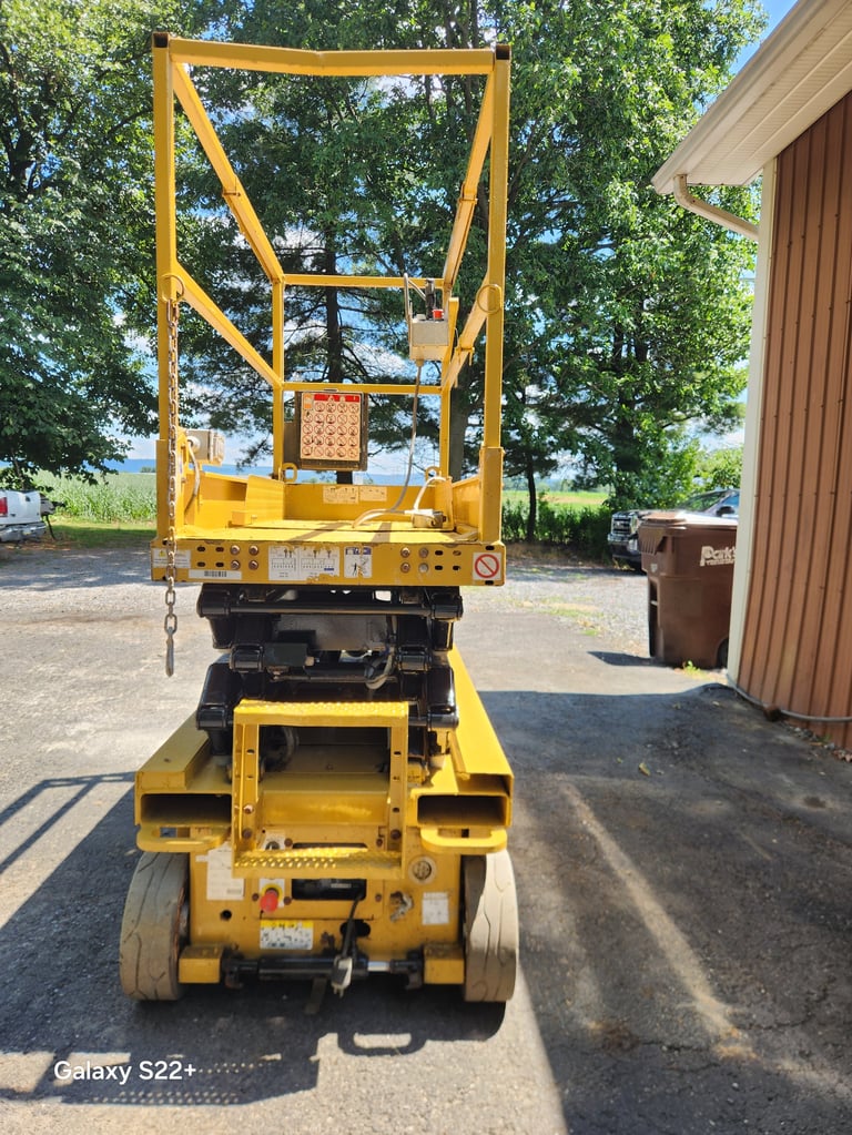 Yellow scissor lift viewed from behind, showing hydraulic platform and extending arms in outdoor storage area