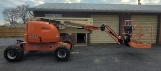Orange boom lift and man lift equipment parked beside a warehouse building