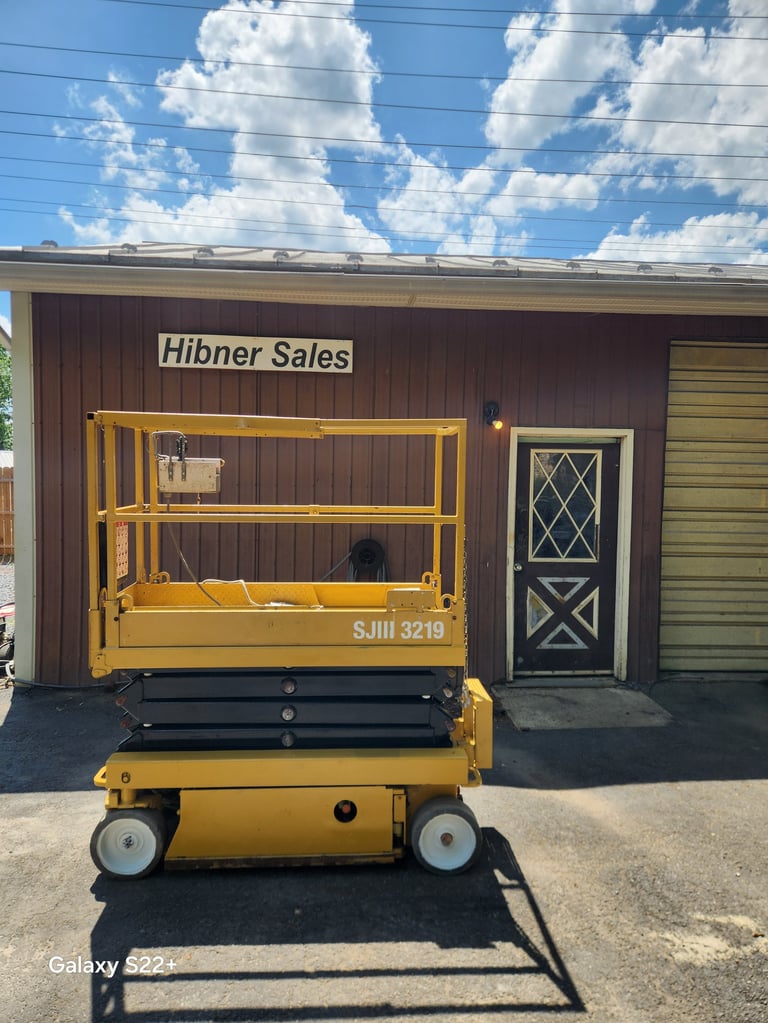 Yellow scissor lift on display outside Hibner Sales building with blue sky and clouds