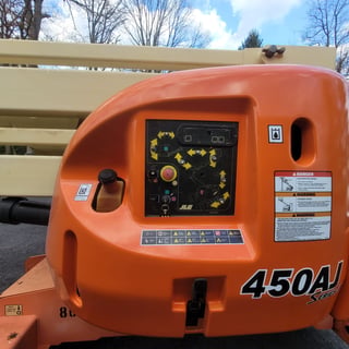 Orange JLG 450AJ lift control panel with yellow directional arrows, warning labels, and emergency stop button